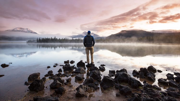 slow travel by a man standing on the bank of a calm lake exhibiting mindful RV living
